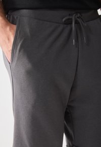 Grå joggebukser laget av myk materiale, med elastisk midje med snor, sidelommer og avslappet passform.