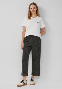 Witte katoenen t-shirt met blauwe grafische tekst, gecombineerd met grijsgroene wijde broek en beige-zwart sneakers met bruine accenten.