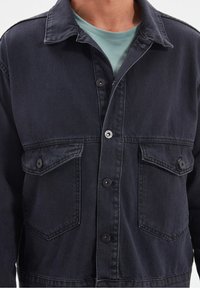 Tmavě modrá džínová bunda s límcem, zapínáním na knoflíky vpředu a dvěma náprsními kapsami. Má dekorativní švy a pohodlný střih.