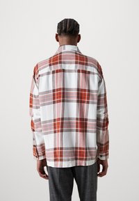 Hedvábná košile s dlouhým rukávem se vzorem kostkované v červených, oranžových a šedých odstínech na bílém podkladu, s límečkem a manžetami na knoflíky. Měkká textilie.