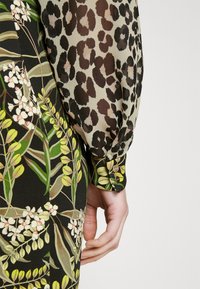 Φόρεμα με μακριά μανίκια που διαθέτει μίγμα λουλουδάτων και λεοπάρ σχεδίων. Το ύφασμα είναι ελαφρύ με διάφανο, υφή μανίκι.