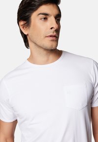 Biała koszulka z krótkim rękawem, wykonana z miękkiej bawełny, z kieszenią na piersi z delikatnym przeszyciem. Okrągły dekolt. Gładka tkanina.