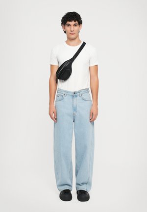 Schwarze Umhängetasche mit einem Reißverschlussfach, getragen über einem schlichten weißen T-Shirt und hellblauen weiten Jeans. Schwarze Schuhe.