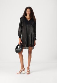 Rochie din satin negru cu mâneci lungi și decolteu în V, cu o croială ușor lejeră. Asortată cu o poșetă neagră și sandale cu toc bloc și bretele albe.