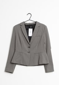 Mustavalkoinen kuvioitu bleiseri, jossa on istuva leikkaus, kaksi etunappia ja peplum-helma. Varustettu lovitetulla kauluksella ja sivutaskuilla.