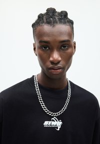 Black sweatshirt featuring a white graphic design at the chest, complemented by a chunky silver chain necklace. Smooth fabric texture.