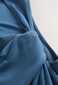 Zila jersey audums ar mezgla dizainu un drapētas tekstūras. Gluda virsma ar redzamām šuvēm, kas izceļ apģērba struktūru.