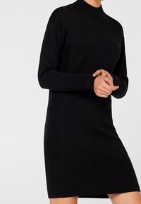 Robe pull noire en tricot avec un col montant, texture côtelée au niveau de l'ourlet et des poignets, présentant des panneaux corporels lisses et une silhouette ajustée.