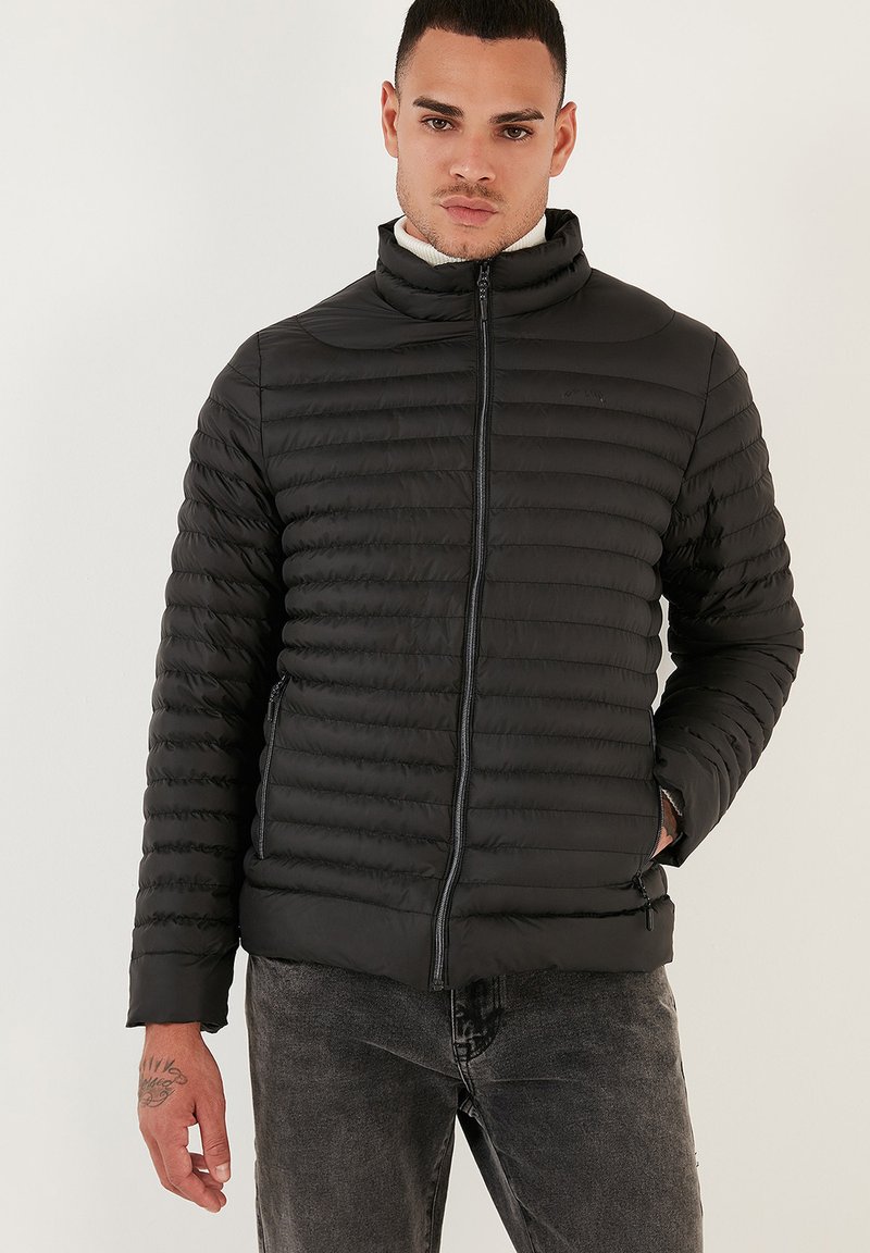 Giacca a vento nera con colletto alto, design trapuntato, chiusura con zip e tasche laterali; realizzata in tessuto liscio e leggero.