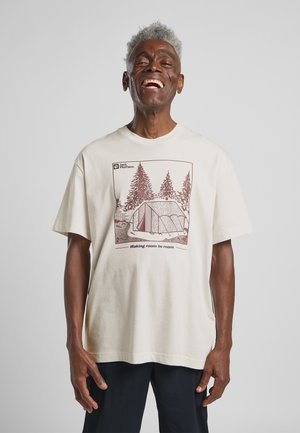 Crème-kleurig katoenen t-shirt met een bruine graphic van een tent en bomen, met de tekst "Making room to roam" en het merklogo. Korte mouwen.