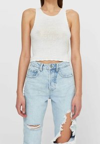 Witte ribgebreide crop top met een ronde halslijn, gecombineerd met high-waisted lichtblauwe jeans met een distressed look en scheuren op de knieën.
