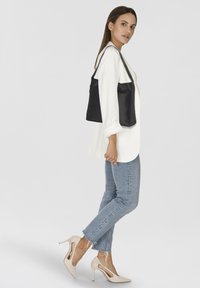 Borsa a spalla nera in pelle con un design semplice, texture liscia e due manici. Indossata con una camicia bianca e jeans azzurri chiari.