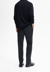 Navy knit sweater with a relaxed fit, paired with black pleated trousers. The look is completed with black shoes.