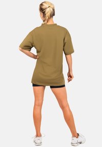 T-shirt oversize verde oliva con maniche corte, realizzato in tessuto morbido. Presenta un collo rotondo e un orlo dritto. Abbinato a pantaloni corti neri.