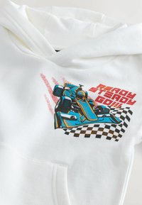 Haut à capuche blanc avec un graphique coloré d'une voiture de course, un motif de drapeau à damiers, et le texte « PRÊT, PARTI, GO !!! » en rouge. Tissu doux, coupe décontractée.