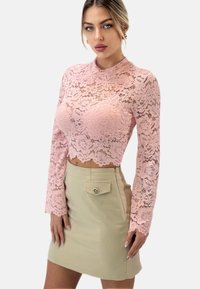 Rosa Spitzen-Crop-Top mit langen Ärmeln und floralem Muster. Kombiniert mit einem khakifarbenen, figurbetonenden Minirock mit einer Fronttasche und Knopfdetails.