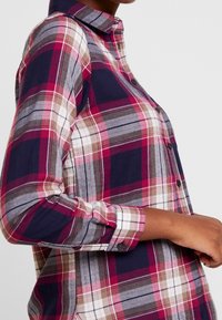 Plaid button-up shirt featuring shades of navy, burgundy, and cream with long sleeves and a classic collar. The fabric appears soft and textured.