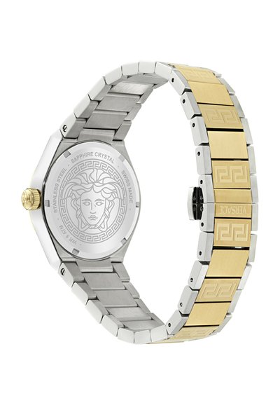 Bracelet de montre en métal bicolore avec des maillons dorés et argentés, des motifs gravés, et un emblème de tête de Méduse sur le fond en acier inoxydable.