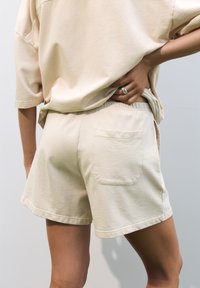 Beige puuvillashortsit rentoa mallia, joissa on joustava vyötärö ja yksi takatasku, esitettynä neutraalilla taustalla.