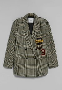Sako s dvojitým zapínáním v černobílém houndstooth vzoru, s vyšívanými nášivkami v žluté, červené a modré barvě a černými knoflíky.