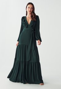 Long green dress in soft fabric; features a v-neckline, ruffled accents, long sleeves, and a tiered skirt with a tied waist.