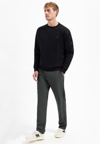 Zwart sweatshirt met geribbelde boorden en halslijn, gecombineerd met donkergroene, slim-fit broek met zijzakken en een gladde textuur.