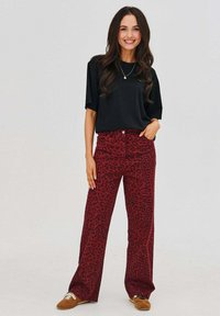 Čierny krátky rukáv top s okrúhlym výstrihom, kombinovaný s širokými červenými nohavicami s čiernym leopardím potlačou.