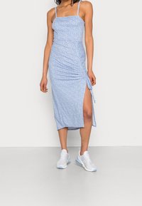 Světle modré midi šaty s květinovým vzorem, řasenými boky a vysokým rozparkem. Stylizováno s bílými sportovními botami a tenkými ramínky.