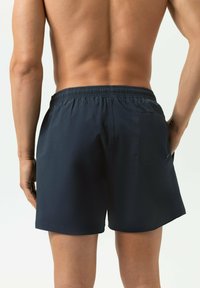 Shorts de bain bleu marine avec une taille élastique et une seule poche arrière, dotés d'un tissu texturé et d'une longueur au-dessus du genou.