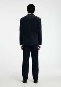 Marinblå kordflamsdräkt med en figursydd kavaj och raka byxor. Tyget har en mjuk textur, och kavajen har en sned krage.