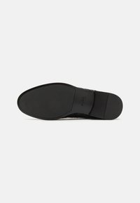 Black leather dress shoe sole with a smooth, flat design. Features subtle branding and a textured pattern for grip. Simple and minimalistic shape.
