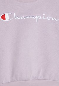 Sudadera morada con dobladillo y puños acanalados, que presenta un logotipo bordado en blanco de "Champion" y un diseño de acento en rojo y blanco.