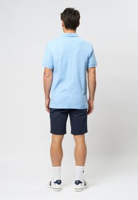 Light blue short-sleeve polo shirt, navy shorts, white socks, and casual shoes with accent details. Fabric appears soft, smooth, and breathable.