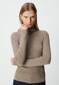 Geribbelde coltrui in een lichtbruine kleur, met lange mouwen en een aansluitend ontwerp, gemaakt van een zacht textielmateriaal.