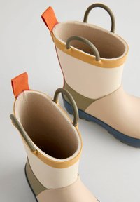 Bottes de pluie en caoutchouc de couleur beige, verte et orange. Caractéristiques : texture lisse, poignées circulaires et semelle extérieure bleue.