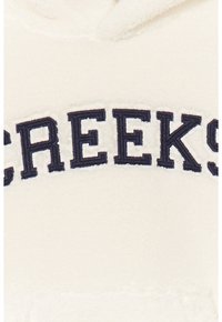 Pullover in pile color crema con scritta ricamata curva in blu navy "CREEK" sul davanti, caratterizzato da una superficie morbida e testurizzata.