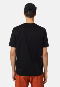 Černé tričko s krátkým rukávem a kulatým výstřihem, hladká textura a minimalistický design. Kombinované s oranžovými texturovanými šortkami, bez výrazných log.