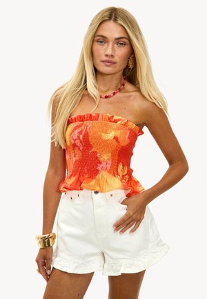 Gestufter trägerloser Tops in lebhaftem Orange mit Blumenmustern, ausgestellt am Saum, kombiniert mit weißen Shorts mit fransigen Kanten.