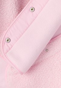 Blødt lyserødt fleece stof med en trykknappanel, der viser teksturerede og glatte sektioner af et beklædningsgenstand tæt på.