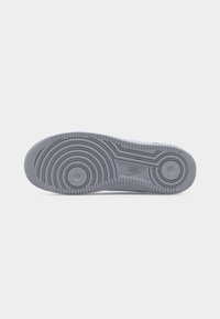 Semelle d'une chaussure Nike gris avec des motifs circulaires et le logo Nike au centre, sur un fond blanc.