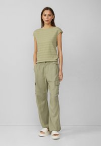 Haut vert clair texturé à manches courtes associé à un pantalon cargo vert clair ample. Présente des poches latérales et une fermeture à bouton. Porté avec des sandales blanches à plateforme.