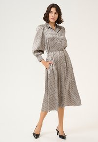 Grijze jurk met stippen, met een knoopsluiting aan de voorkant, een cinched taille en ballonsleeves. Glad textuur, tot de knie, gecombineerd met zwarte slingback hakken.