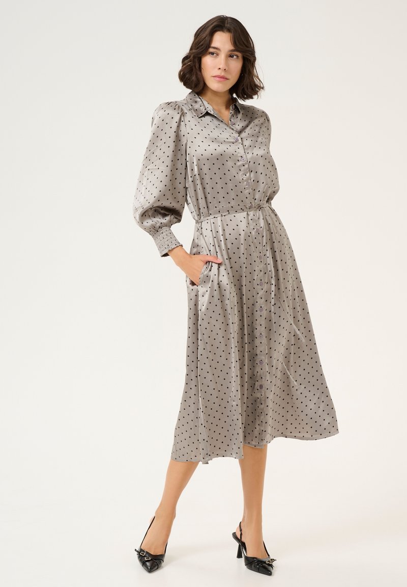 Grijze jurk met stippen, met een knoopsluiting aan de voorkant, een cinched taille en ballonsleeves. Glad textuur, tot de knie, gecombineerd met zwarte slingback hakken.