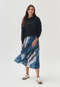 Marineblå sweatshirts med hætte, parret med en plisseret midiskirt i et blåt og hvidt abstrakt mønster, suppleret med hvide sneakers.