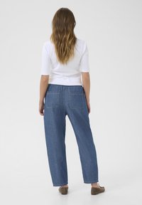 Afslappede, højtaljede blå denimbukser med elastisk talje og to baglommer. Bærer en tætsiddende hvid top og flade sko.
