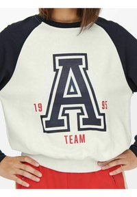 Sudadera blanca con mangas raglán en azul marino, con una gran letra negra "A" y texto rojo "TEAM 1995" en el frente. Textura suave.