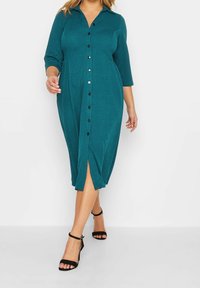 Sukienka na guziki w kolorze morskim, z kołnierzykiem, rękawami do połowy łokcia i długością do połowy łydek. Posiada przedni rozcięcie i czarne guziki.