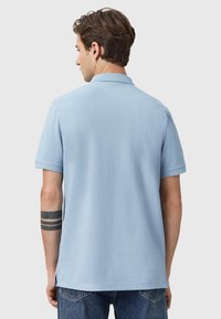 Polo shirt azzurro chiaro realizzato in cotone morbido, con colletto a coste e maniche corte, dotato di spacchi laterali e texture liscia.