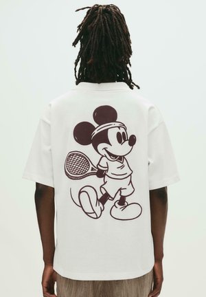 Hvid kortærmet t-shirt med et brunt grafisk motiv af en tegneseriefigur, der spiller tennis på ryggen. Regular fit, lavet af bomuldsmateriale.