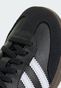 Čierne tenisky vyrobené z ko�že a semišu, s textúrovaným povrchom, okrúhlym prstom, šnúrkami a tromi bielymi cik-cak pruhmi. Gumová podrážka.